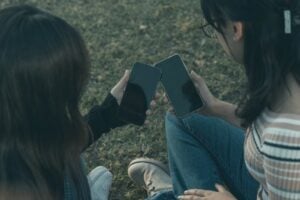 Two women sit outdoors holding smartphones, suggesting love bombing dating apps.