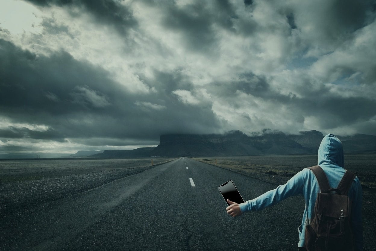 A person with a backpack holding a tablet on a road with a cloudy sky.