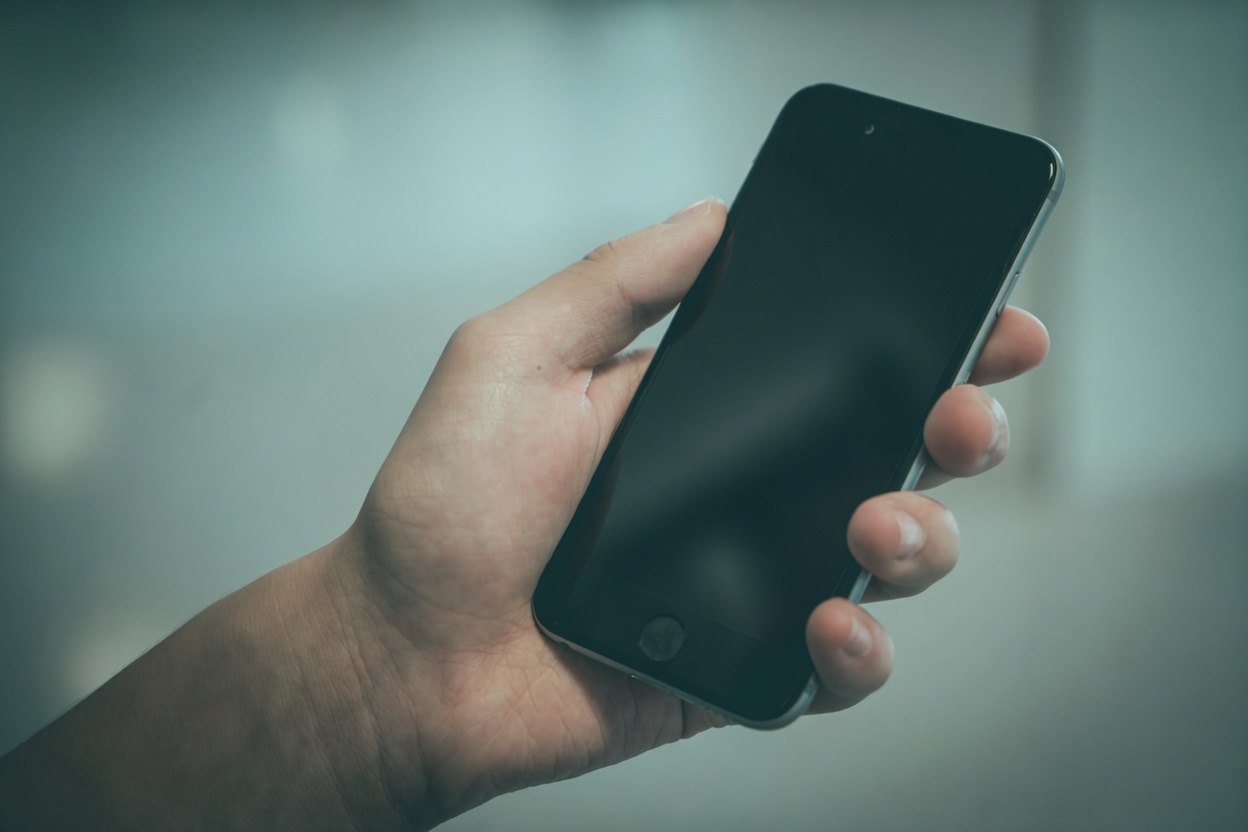 A hand holding a black smartphone with a blurred background.
