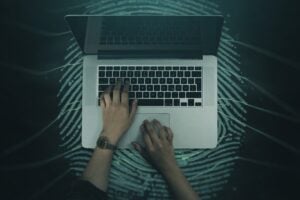 Hands typing on a laptop over a fingerprint pattern for digital fingerprint username search.