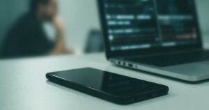 Smartphone on a desk beside a laptop, for search someone on hinge by email.