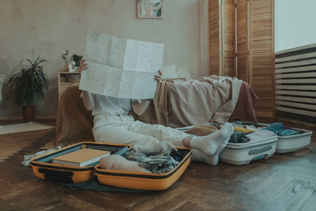 Airbnb Address Lookup Before Booking 1 A person sits on the floor with a map, surrounded by open suitcases and clothes.