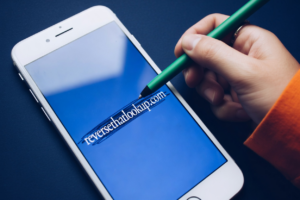 A hand holds a pencil over a smartphone screen for how to tell if someone blocked you on facebook.
