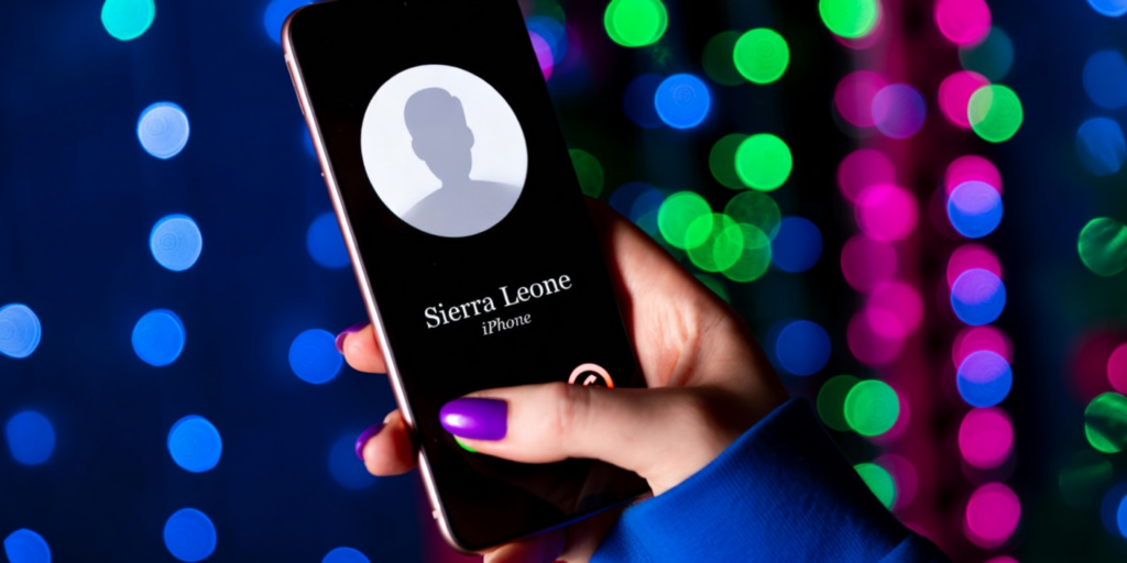 Hand holding a phone with Sierra Leone on screen, illustrating one ring scam.