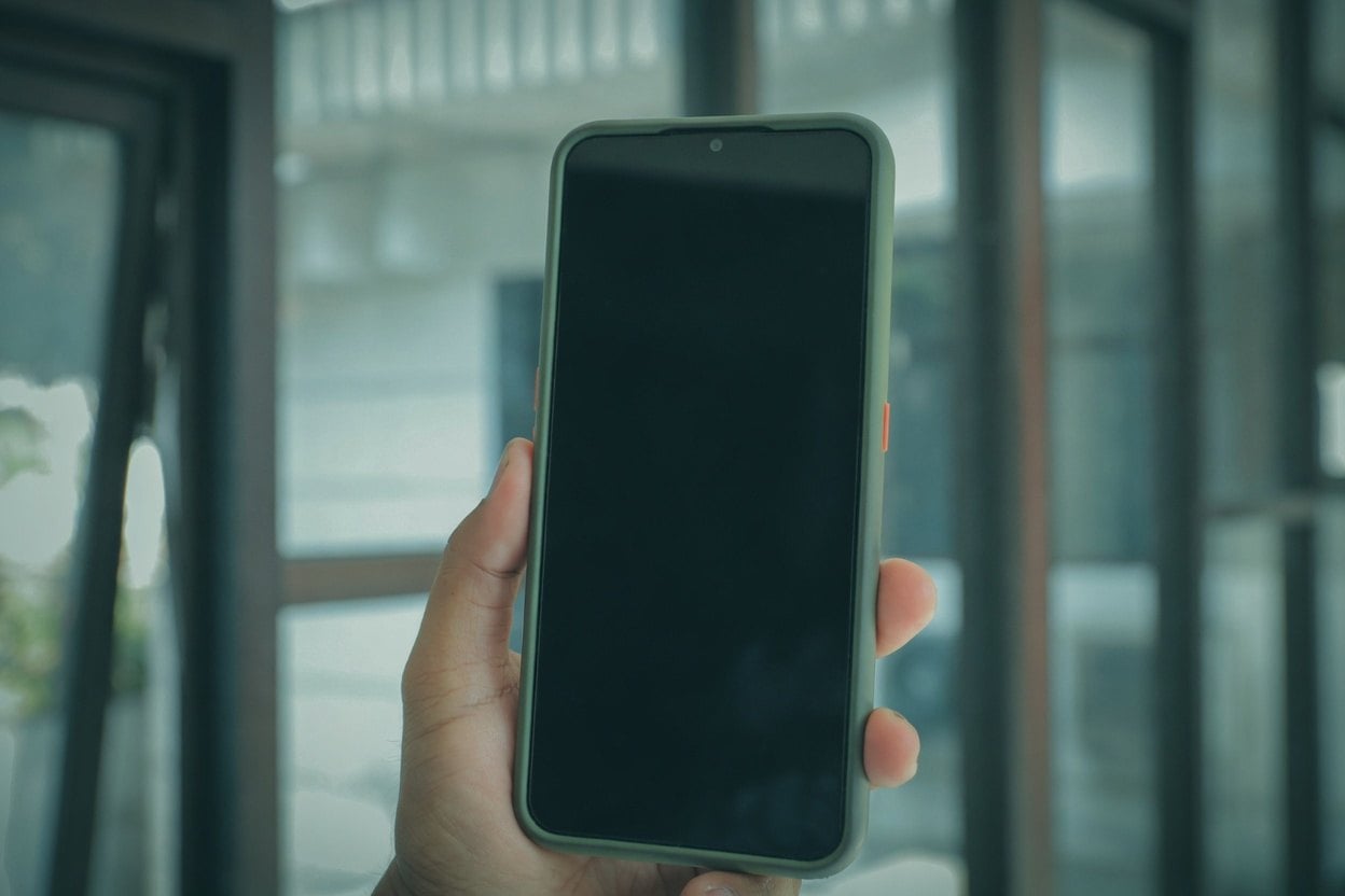 A hand holding a smartphone with a black screen