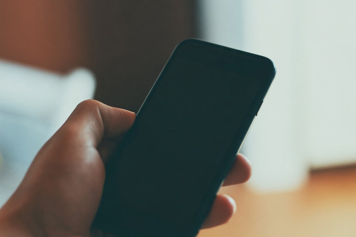 A hand holding a black smartphone with a blurred background