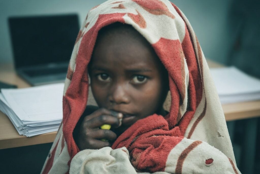 Child wrapped in a blanket sits in front of a laptop, illustrating freeze your child’s credit.