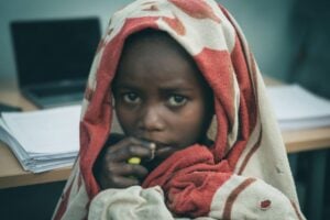 Child wrapped in a blanket sits in front of a laptop, illustrating freeze your child’s credit.
