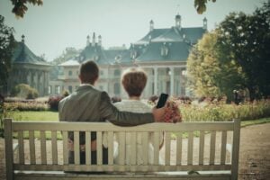 Couple on a bench, holding a phone, at a garden estate for check if partner is married online.