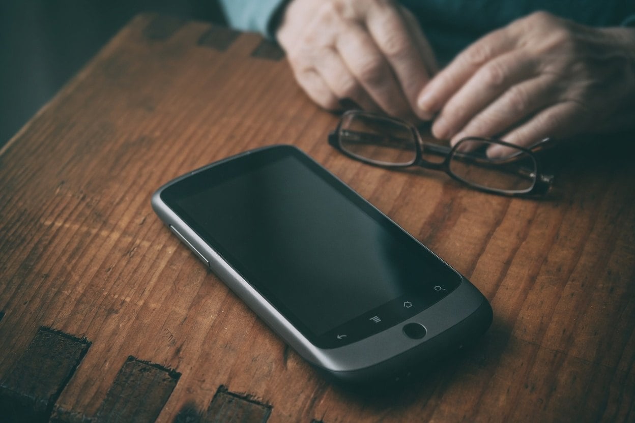 A smartphone and glasses on a wooden table